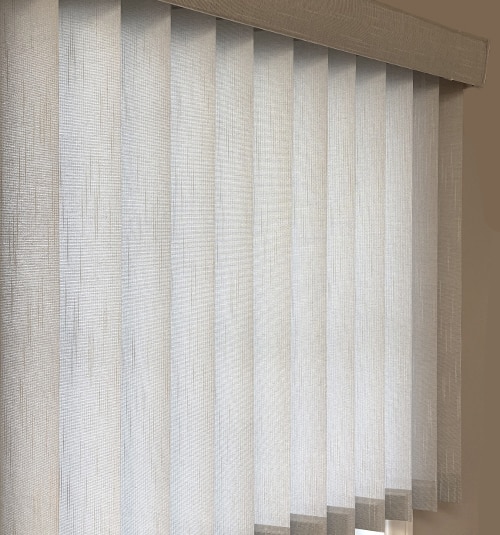 Close up of tilted free hanging fabric vertical vanes and headrail. Shown in Flaxen Light Gray
