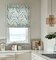 Blue green and white leaf pattern cordless roman shade in a kitchen with white countertops and gold handled white cabinets