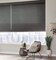 A bohemian room with wicker armless chair in front of large windows with dark gray bamboo woven shades overlooking a city